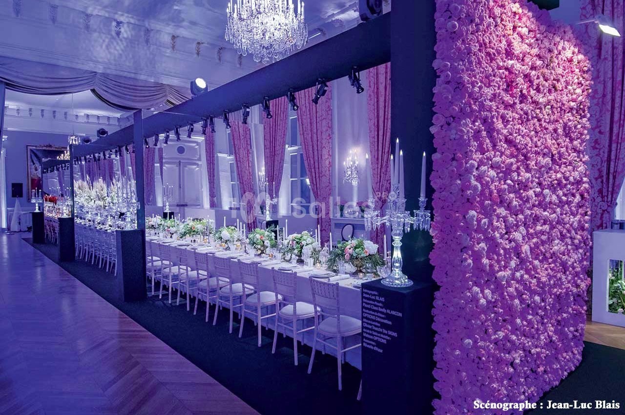 Salle de réception élégante avec une longue table décorée de fleurs et un mur couvert de roses roses.