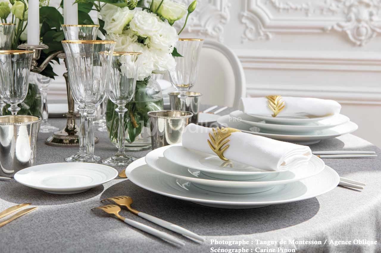 Table élégamment dressée avec vaisselle blanche, couverts dorés, verres en cristal et décorations florales blanches.