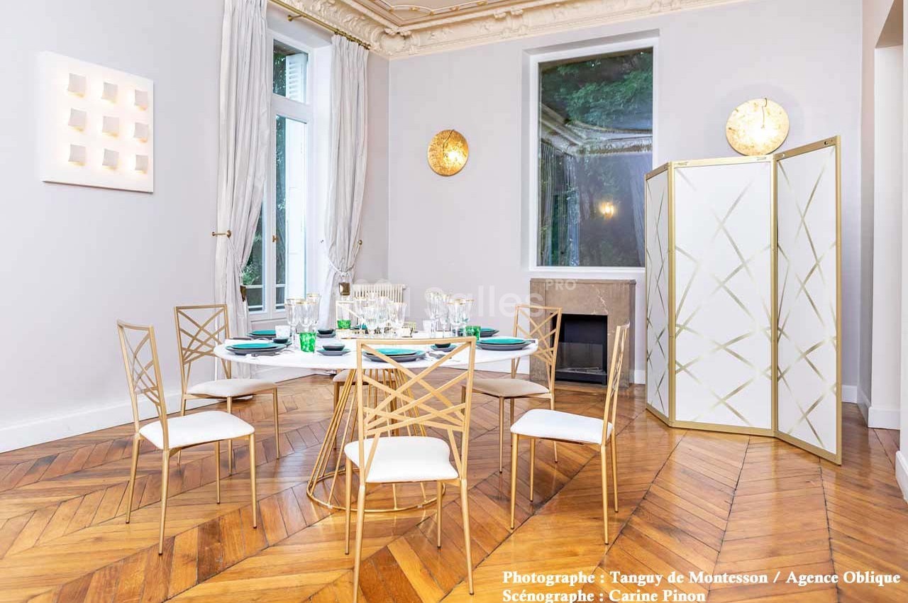 Salle à manger élégante avec parquet en chevrons, table dressée, chaises dorées et paravent décoratif.