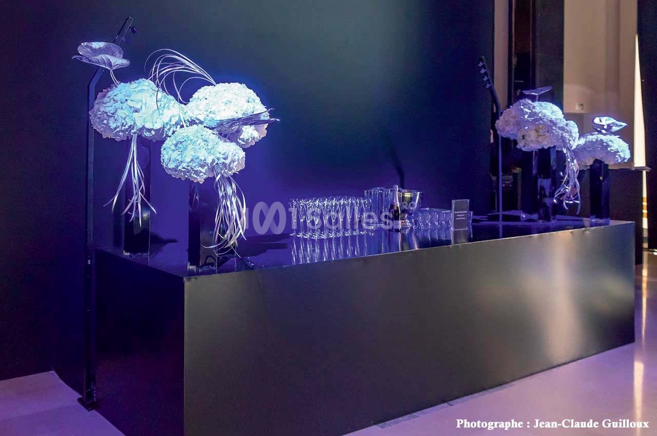 Table noire élégante décorée de bouquets blancs et de verres alignés, éclairée par une lumière violette.