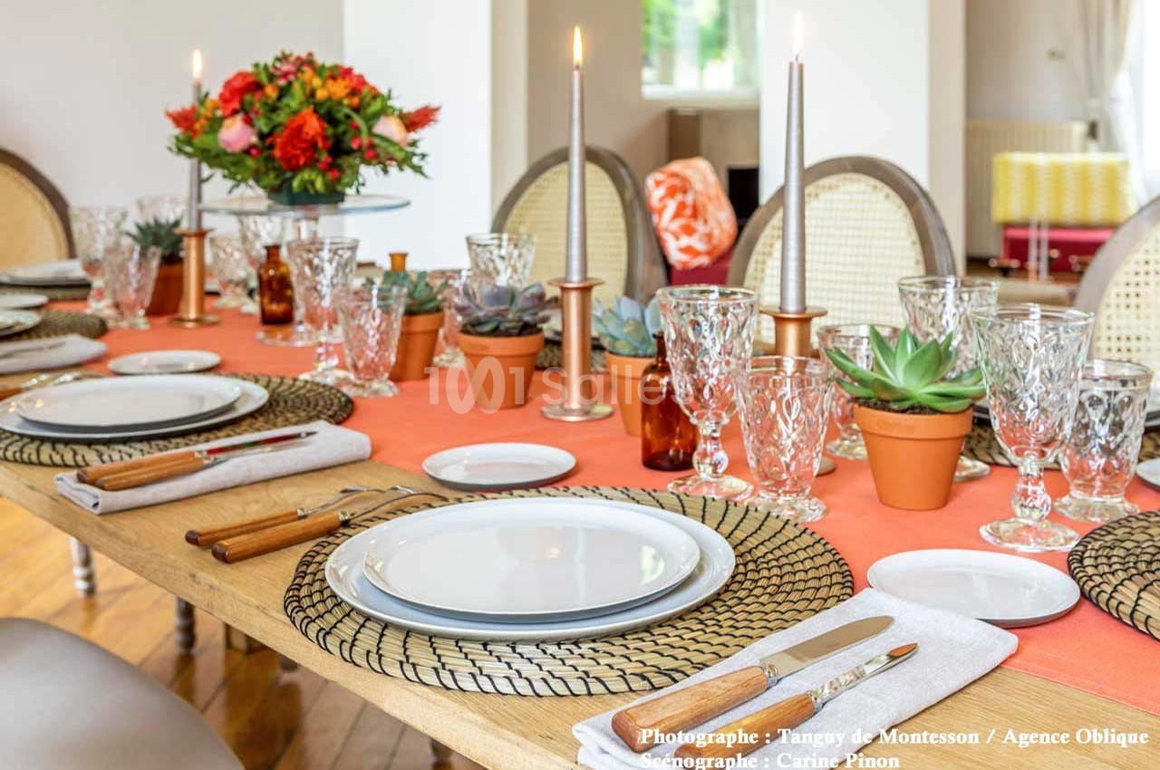 Table élégamment dressée avec assiettes blanches, verres en cristal, bougies allumées et décoration florale colorée.