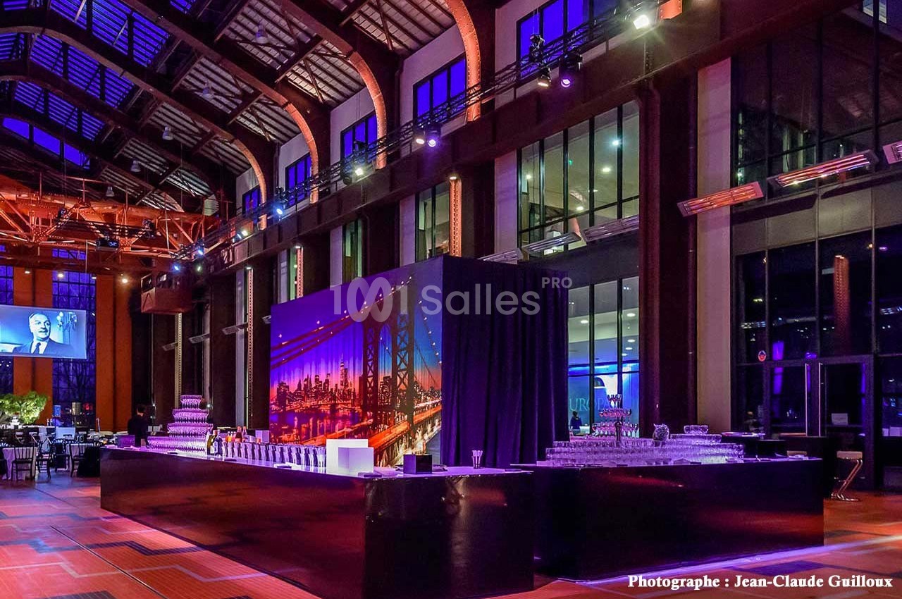 Salle de réception spacieuse avec éclairage coloré, grande table de buffet et décor urbain en arrière-plan.