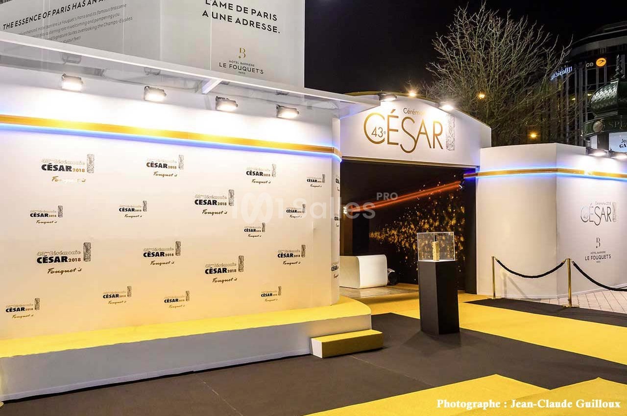 Entrée d'une cérémonie avec tapis jaune, mur de logos ’César’ et décor lumineux en arrière-plan.