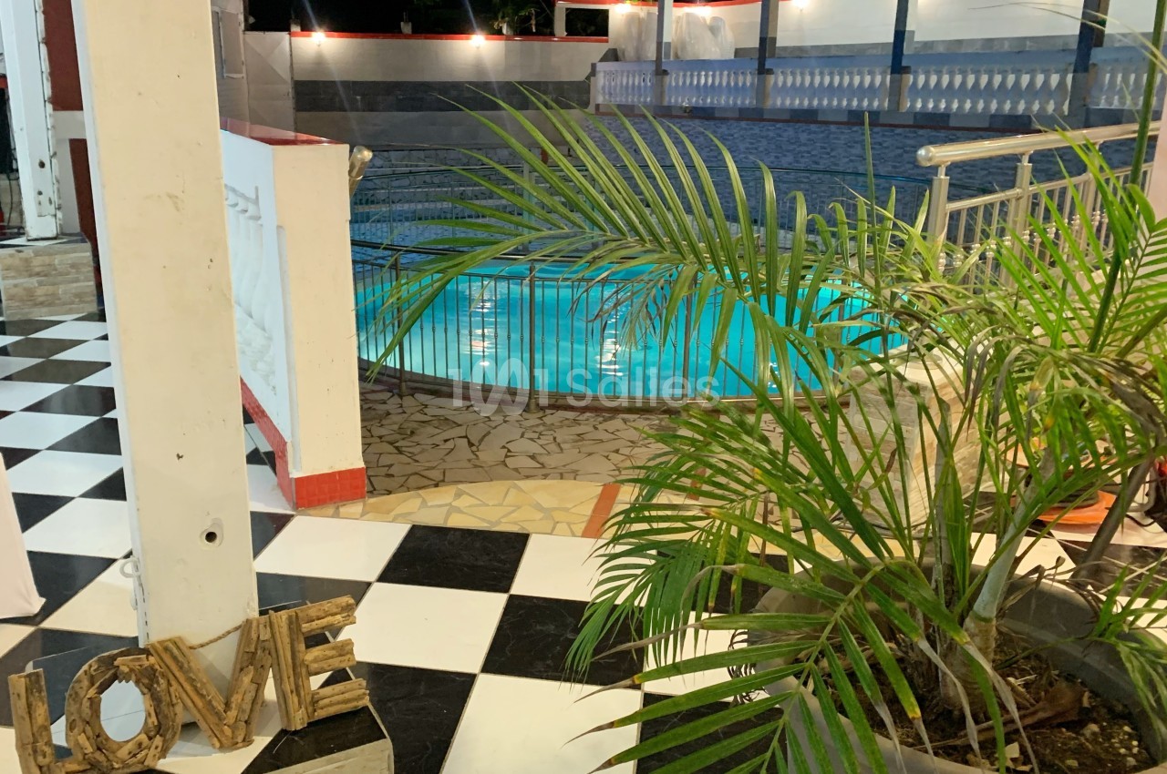 Piscine éclairée de nuit avec carrelage noir et blanc, plante en pot au premier plan et décoration ’LOVE’ en bois.