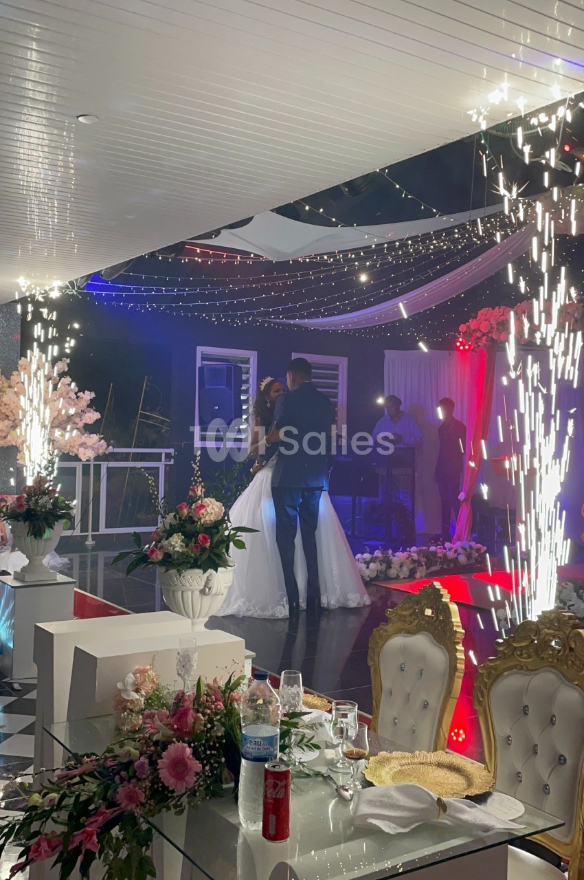 Un couple danse sous des étincelles lors d'une réception de mariage dans une salle décorée de fleurs et de lumières.