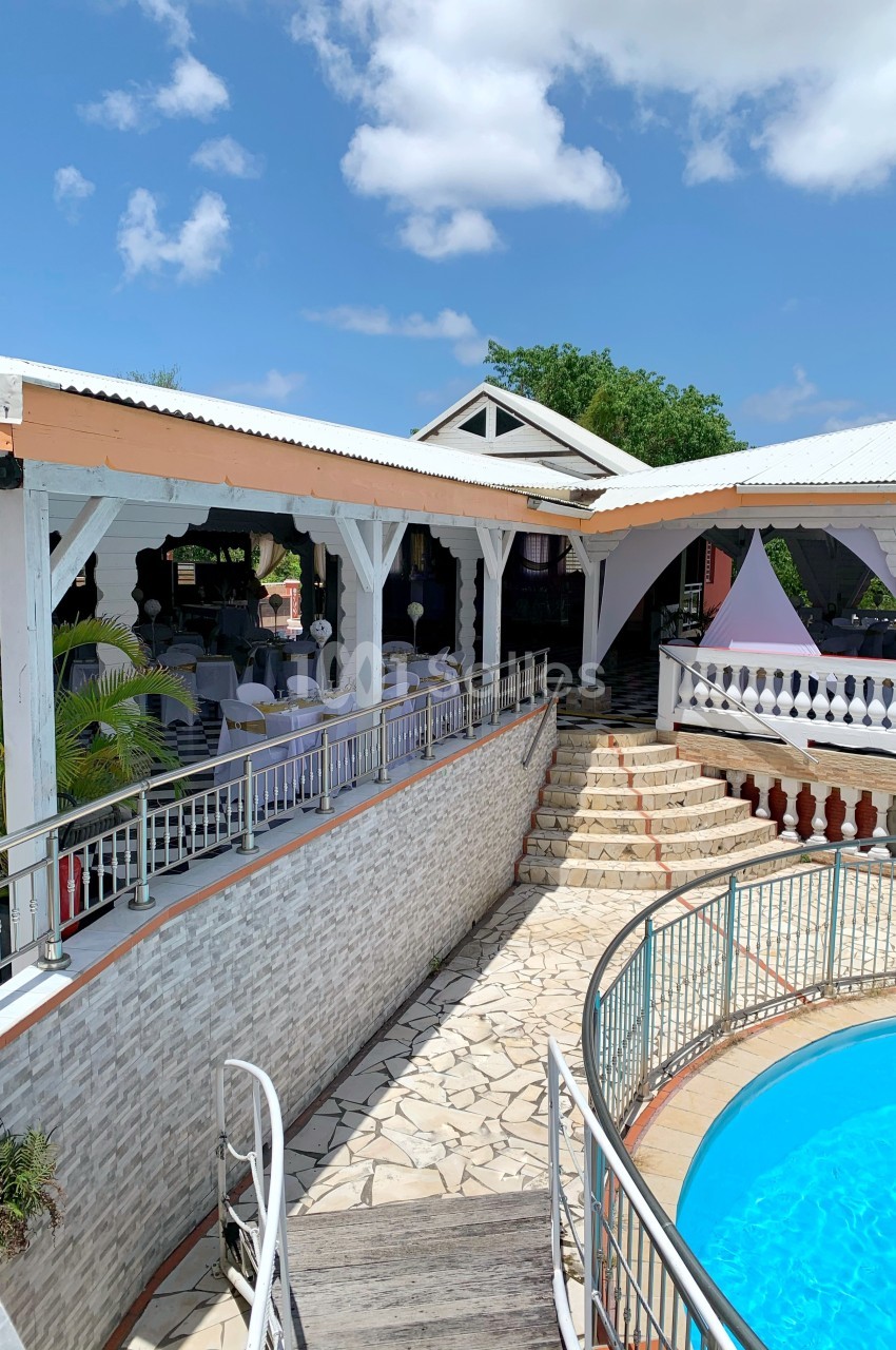 Terrasse extérieure avec tables dressées, escalier en pierre, piscine ronde et ciel dégagé en arrière-plan.