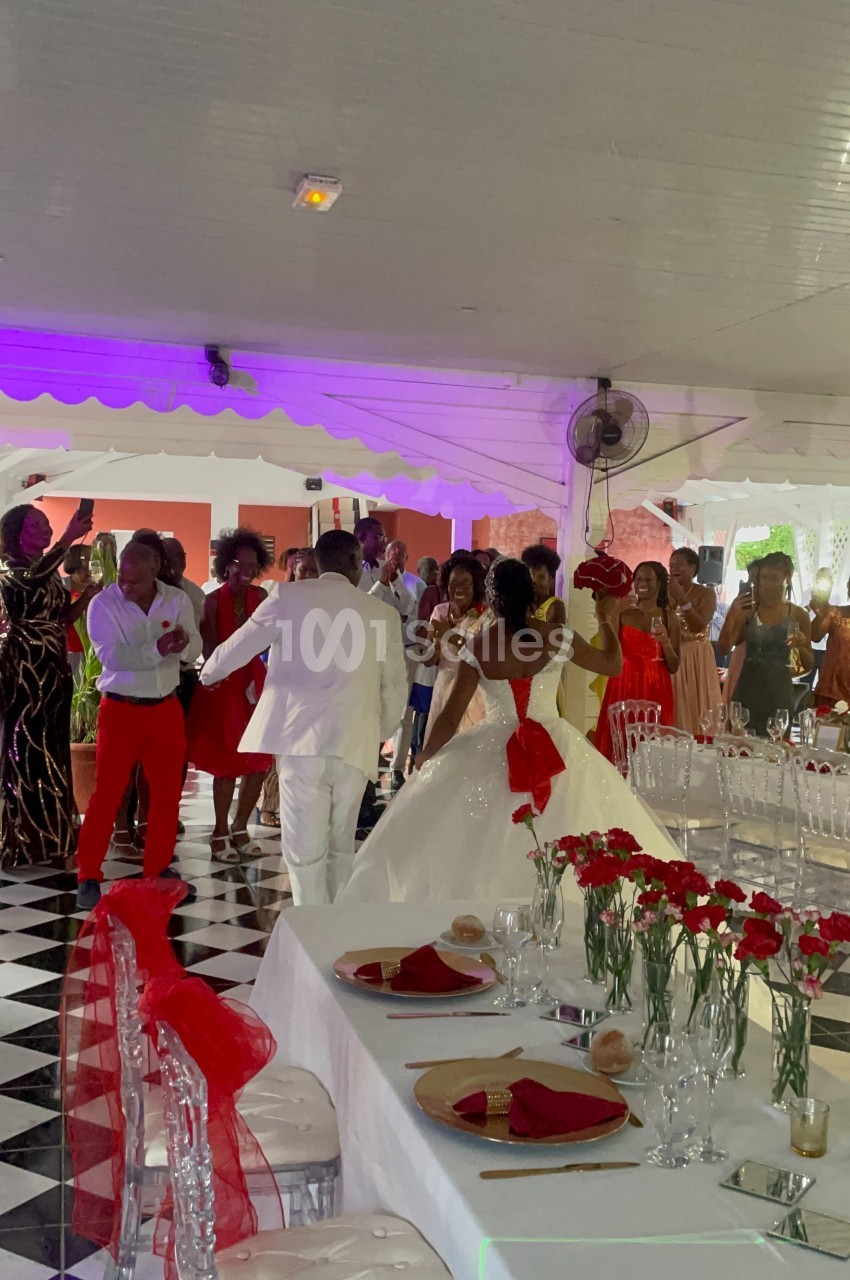 Un couple de mariés danse au centre d'une salle décorée, entouré d'invités applaudissant.