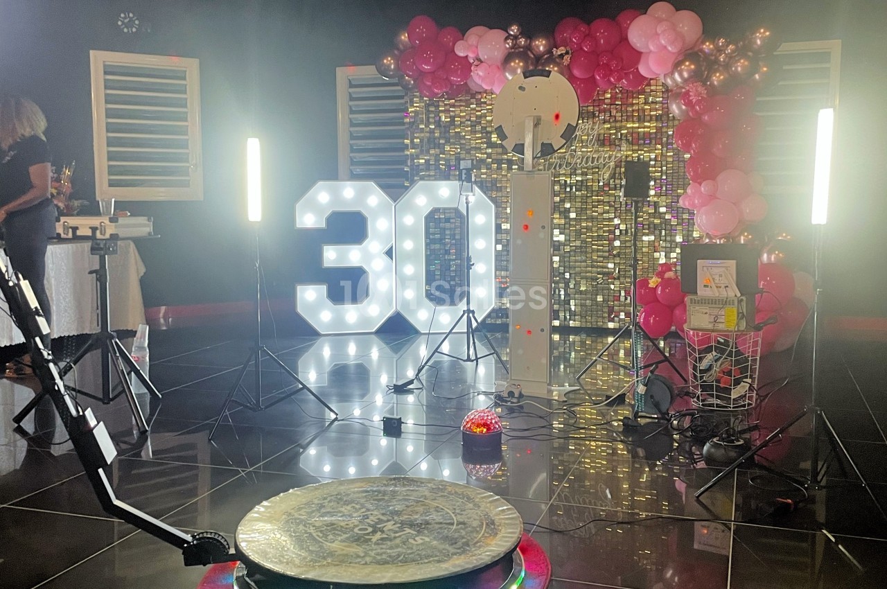 Décoration festive avec ballons roses, chiffre lumineux ’30’, fond scintillant et équipement de photographie.