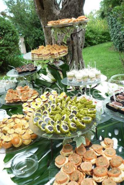 Buffet en extérieur avec une variété de plats salés et sucrés disposés sur des plateaux décorés de feuilles tropicales.