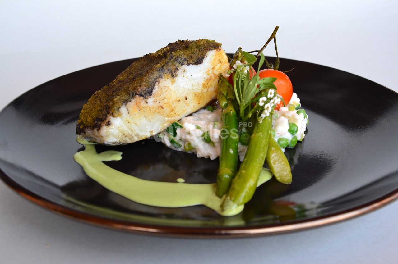 Filet de poisson avec croûte d'herbes, servi sur risotto aux légumes et sauce verte, décoré de légumes frais.