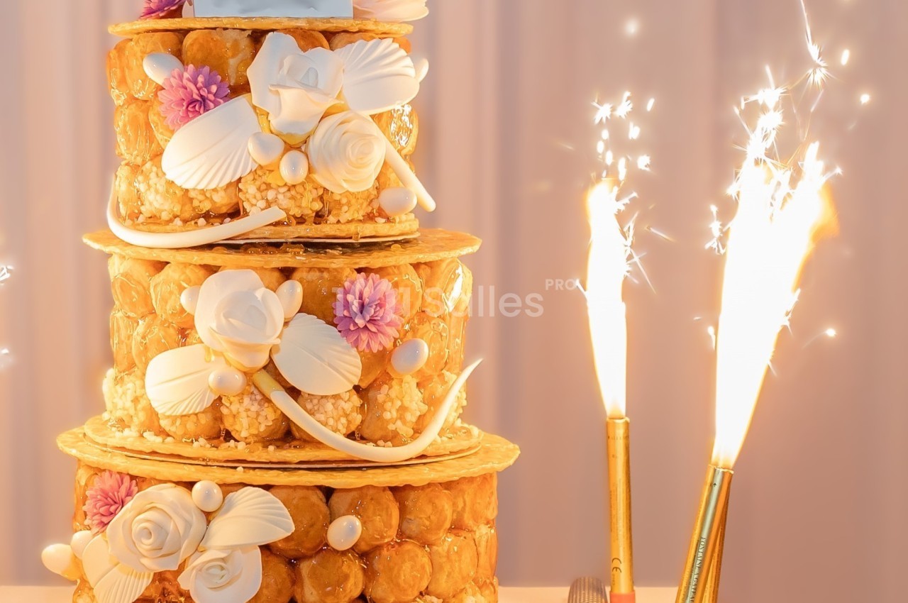 Pièce montée en choux décorée de fleurs en sucre, avec des cierges magiques allumés sur le côté.