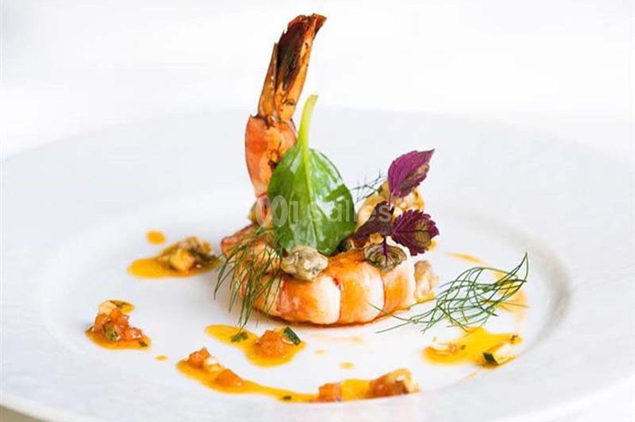 Crevette dressée sur une assiette avec sauce, herbes fraîches et feuilles décoratives.