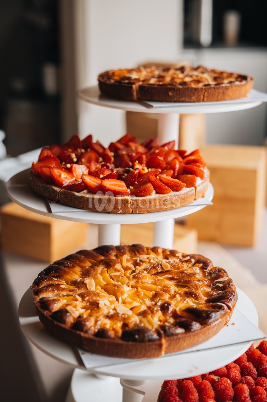 Trois tartes aux fruits, dont une aux fraises et une aux abricots, présentées sur des plateaux blancs empilés.