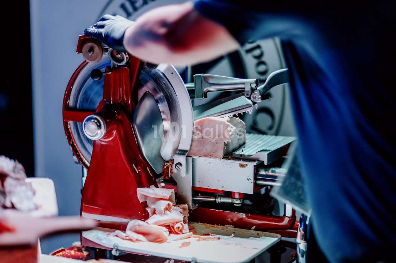 Personne utilisant une trancheuse rouge pour couper de la charcuterie dans un environnement professionnel.