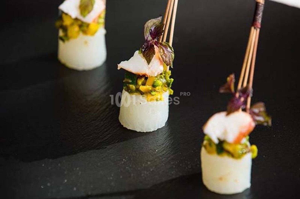 Bouchées gastronomiques composées de poisson, légumes et herbes, présentées sur une assiette noire.