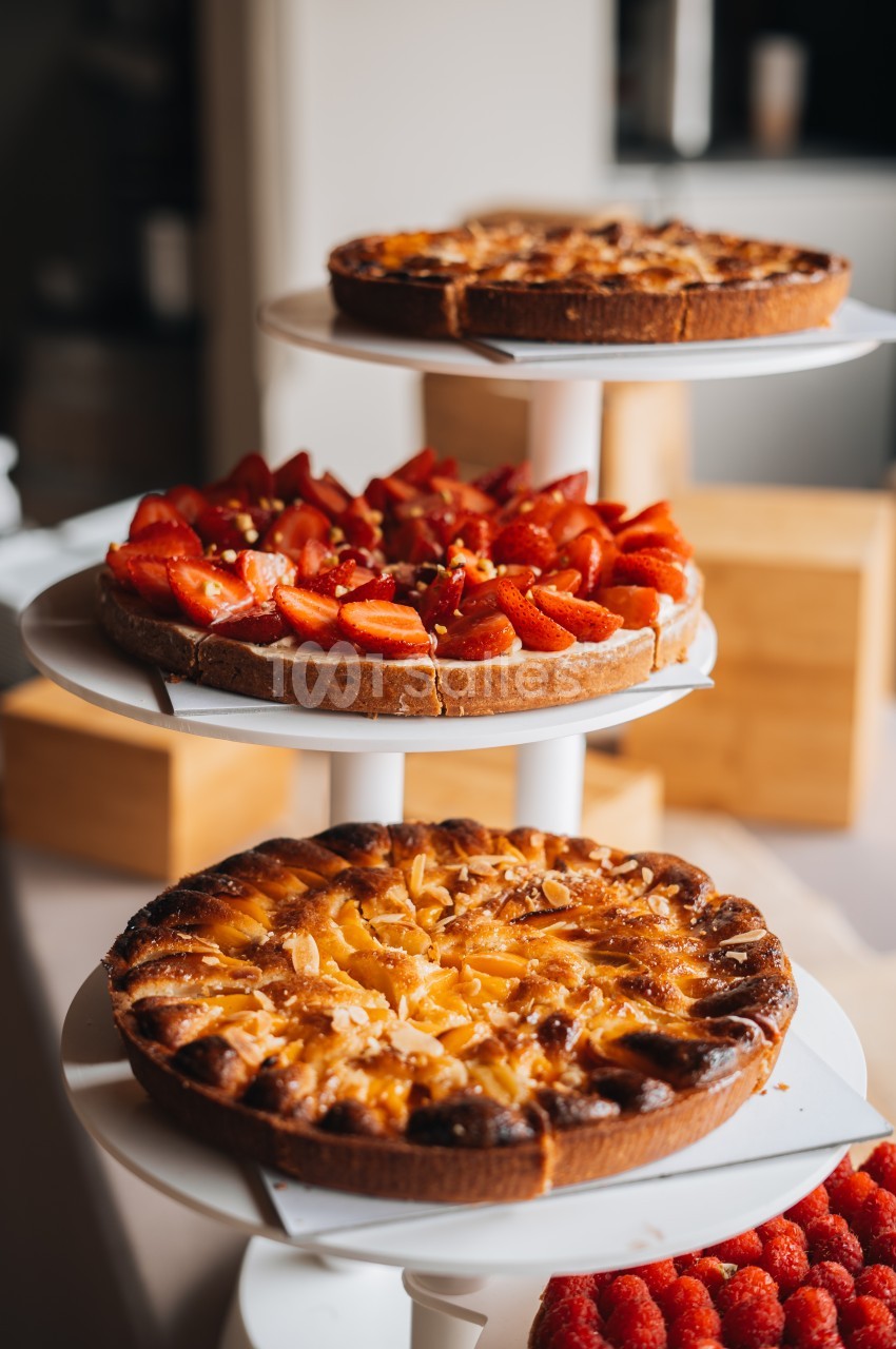 Trois tartes aux fruits, dont une aux fraises et une aux abricots, présentées sur des plateaux blancs empilés.