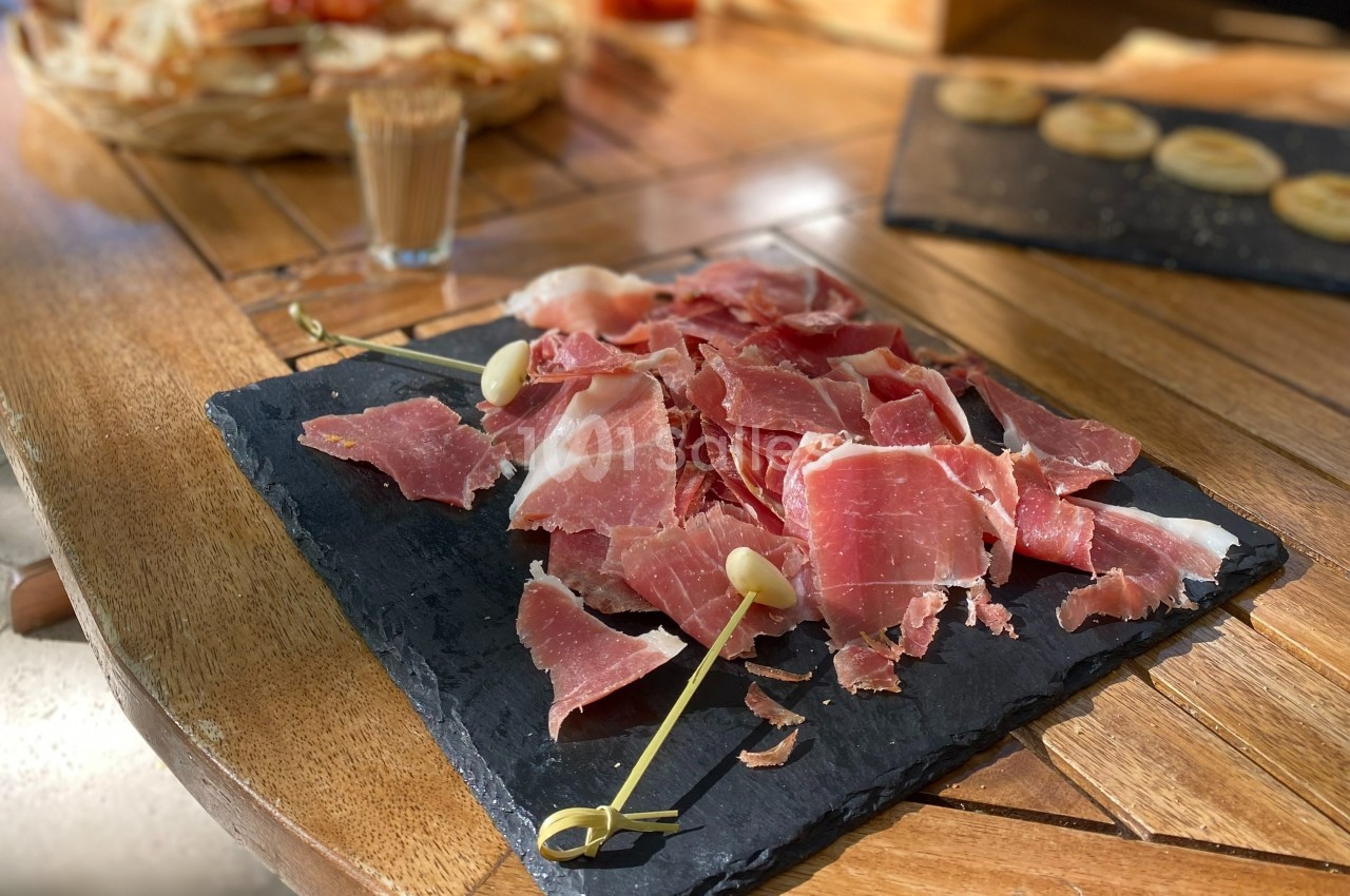 Assiette d'ardoise garnie de tranches fines de jambon cru, accompagnée de piques en bois sur une table en bois.