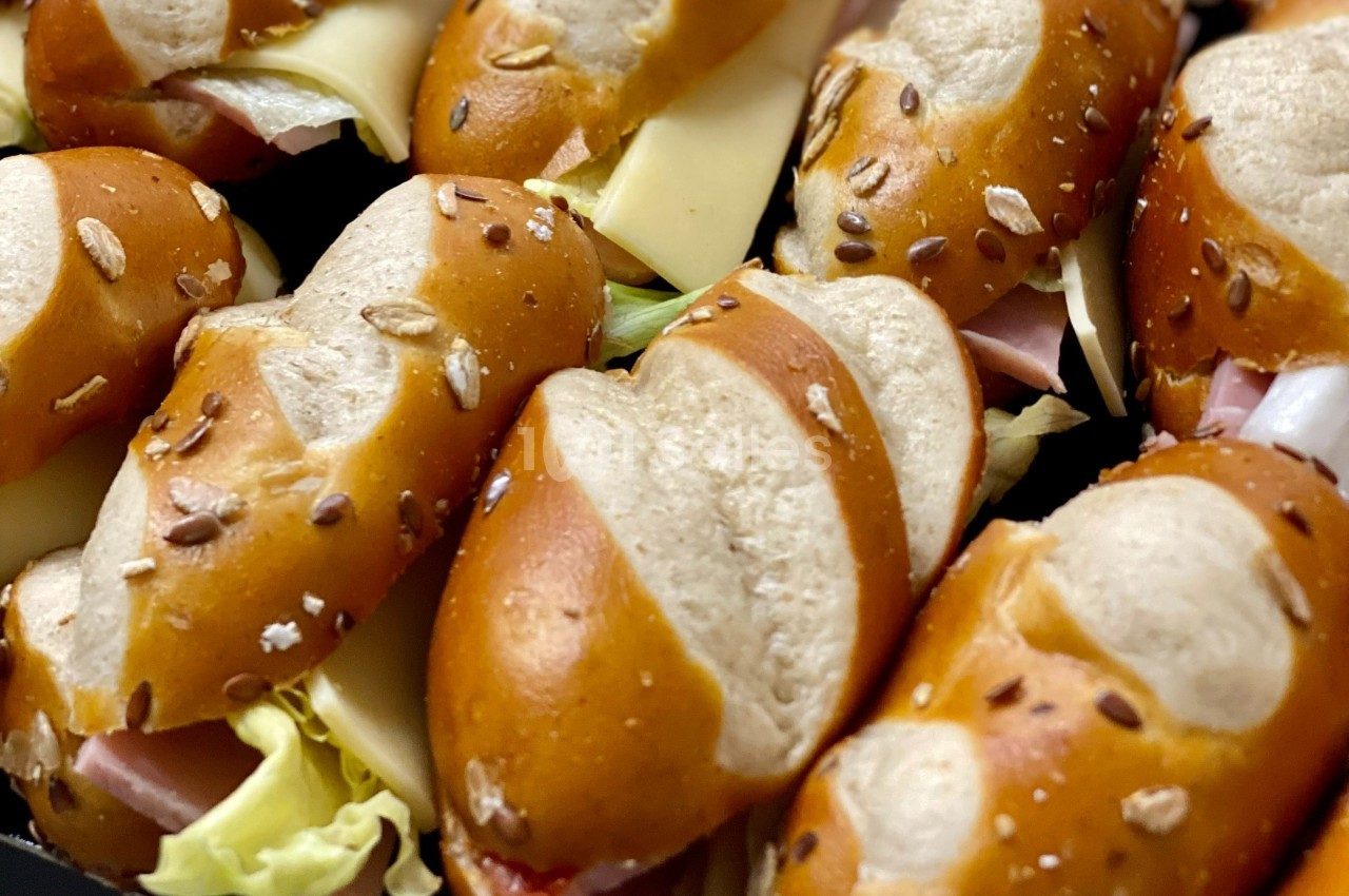 Petits sandwichs au pain bretzel garnis de fromage, jambon, laitue et graines sur le dessus.