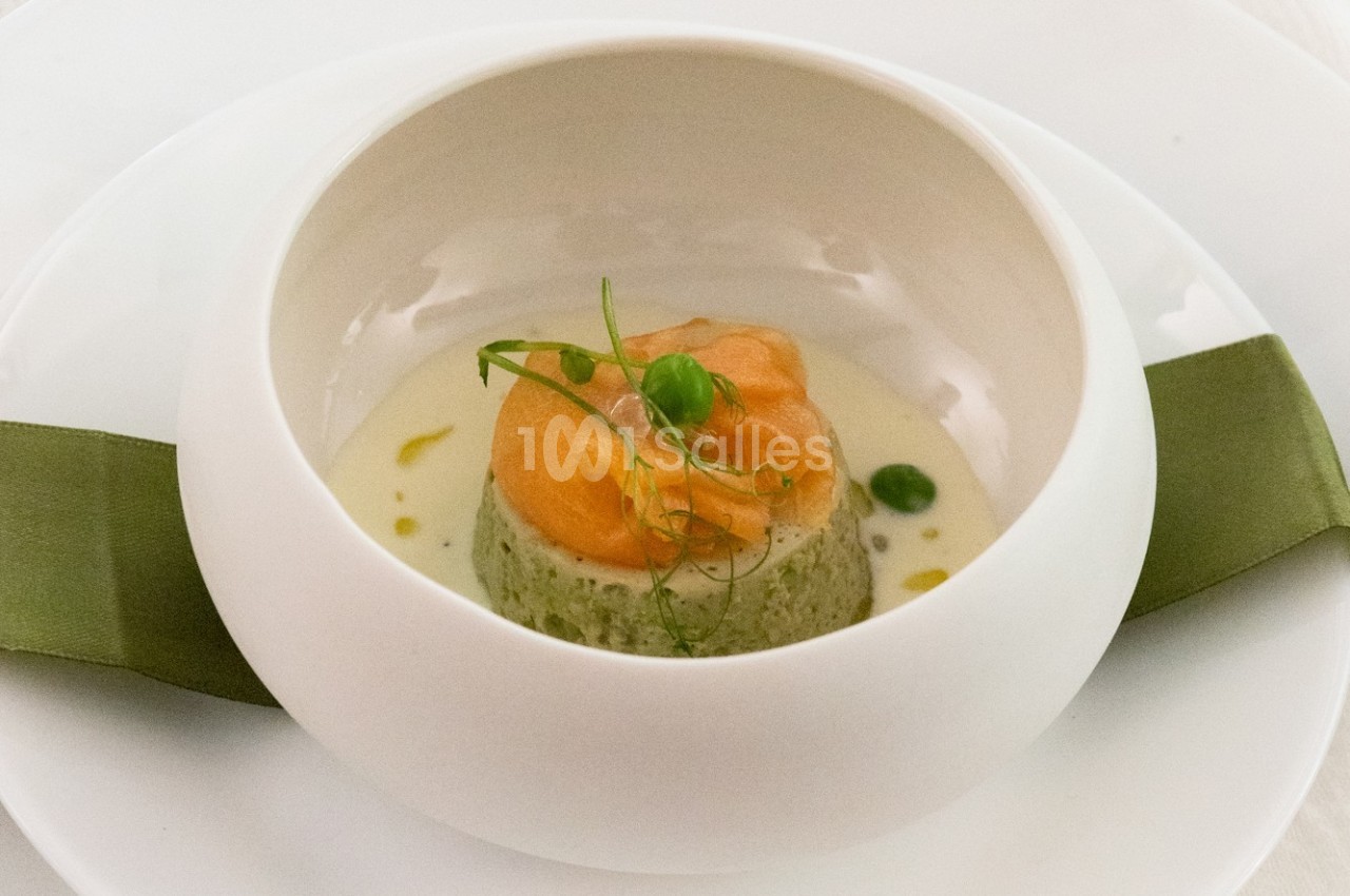 Plat gastronomique composé d'une mousse verte, surmontée de saumon et de pousses, présenté dans une assiette blanche.
