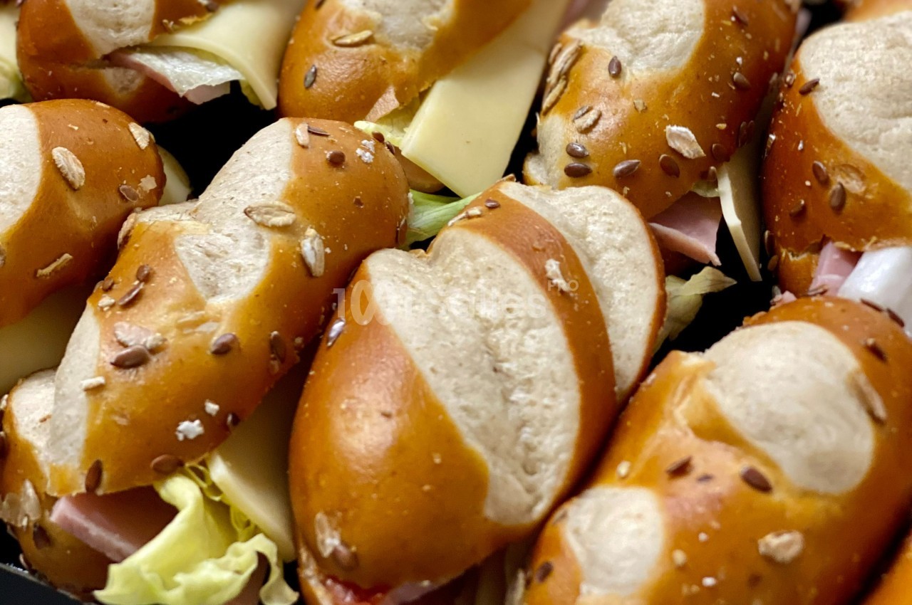 Petits sandwichs au pain bretzel garnis de fromage, jambon, laitue et graines sur le dessus.