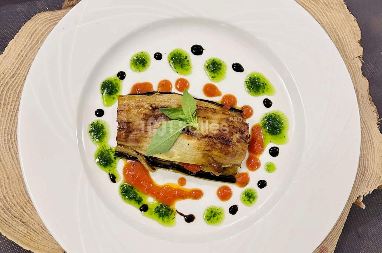 Assiette garnie d'un plat à base d'aubergine grillée, décorée de sauces colorées et d'une feuille de basilic.