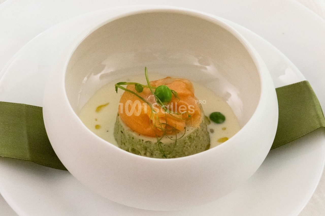 Plat gastronomique composé d'une mousse verte, surmontée de saumon et de pousses, présenté dans une assiette blanche.