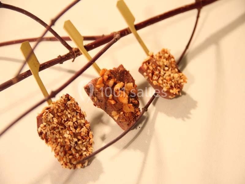 Trois bouchées chocolatées enrobées de noisettes concassées, présentées sur des branches en bois.