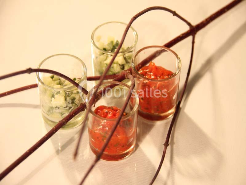 Quatre verrines contenant des préparations colorées, rouges et vertes, décorées de branches fines sur une table blanche.