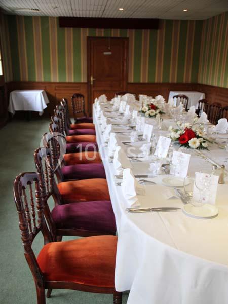 Table dressée avec nappes blanches, couverts, menus et décoration florale, entourée de chaises en bois dans une salle…