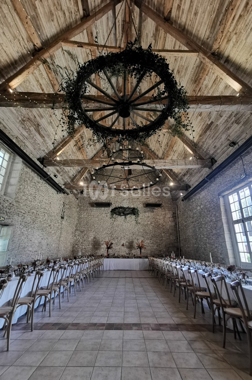 Salle de réception en pierre avec plafond en bois, tables décorées et suspensions végétales circulaires.