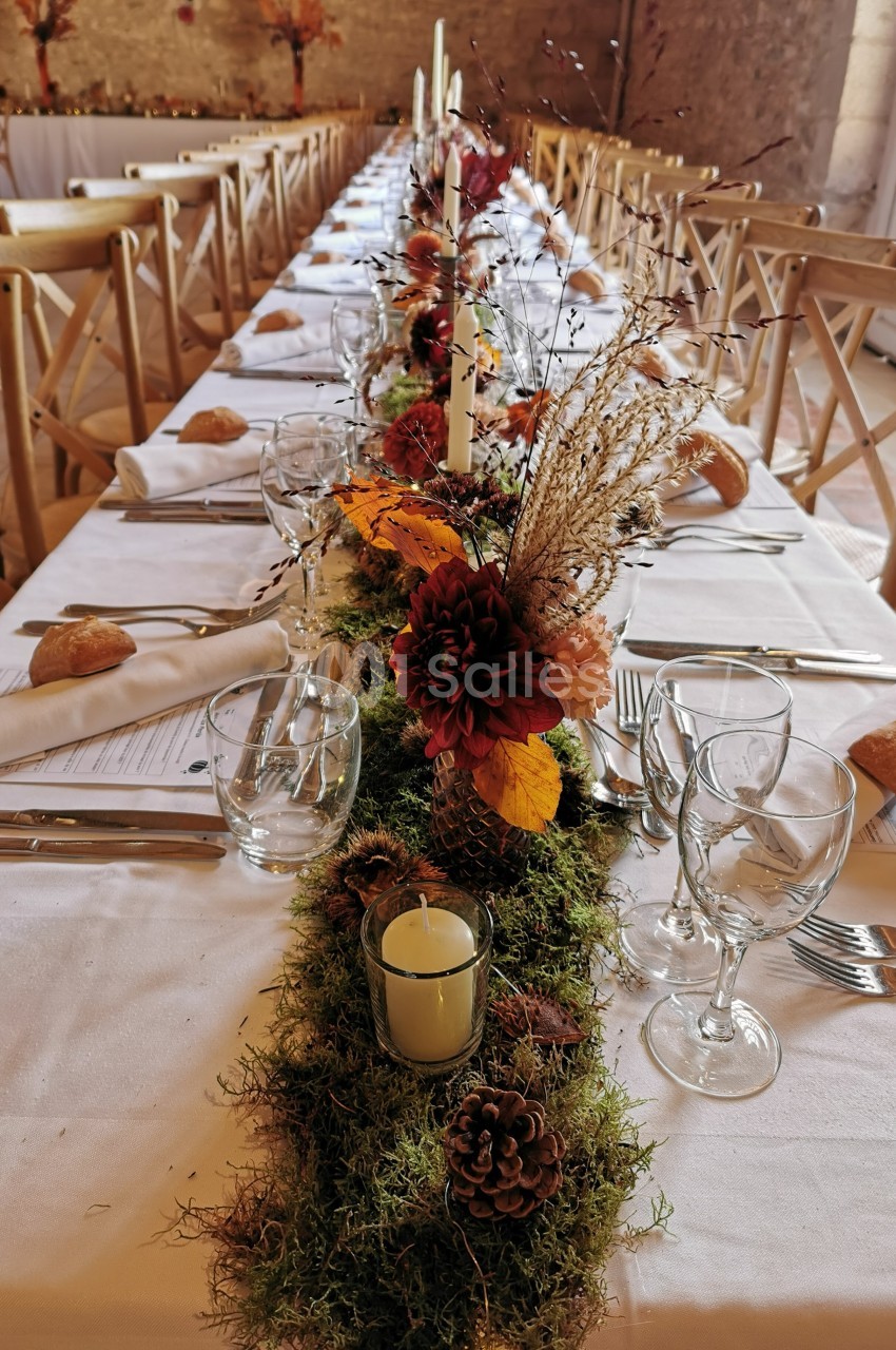 Table de banquet décorée avec des fleurs automnales, des bougies et de la mousse, entourée de chaises en bois.