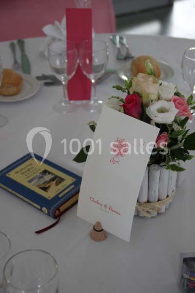 Centre de table avec bouquet de fleurs, menu imprimé et livre posé sur une nappe blanche.