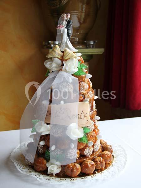 Pièce montée en choux décorée de fleurs en sucre, ruban blanc et figurines de mariés au sommet.