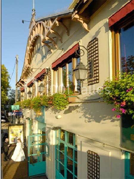 Façade d'un bâtiment avec des fenêtres à volets rouges, des jardinières fleuries et une entrée vitrée.