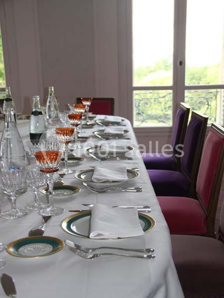 Table dressée avec nappes blanches, vaisselle élégante, verres et chaises colorées devant une fenêtre lumineuse.