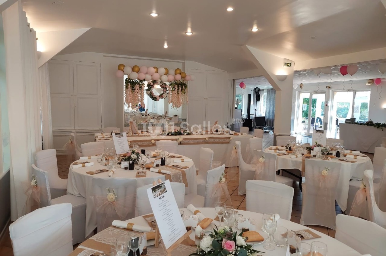Salle de réception décorée pour un mariage, avec tables dressées, nappes blanches et ornements floraux.