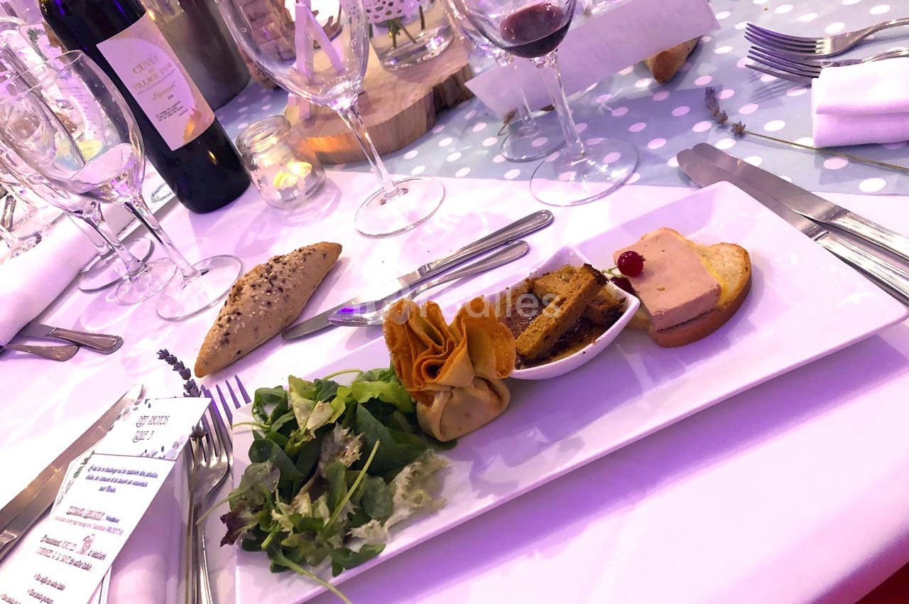 Assiette de mise en bouche avec salade, pain, feuilleté, foie gras et verre de vin sur une table dressée.