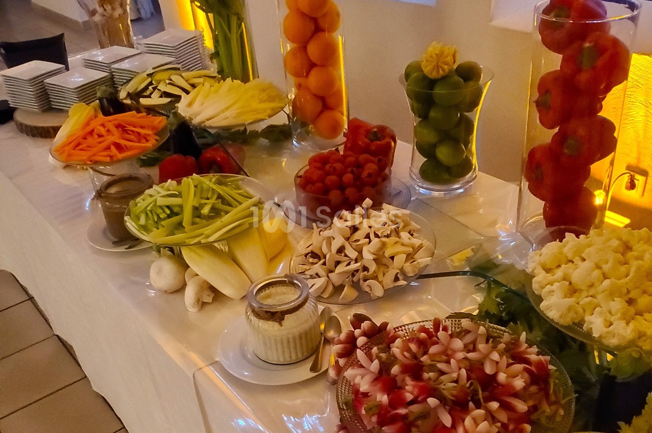 Buffet de légumes frais variés disposés sur une table, accompagnés de sauces et présentés dans des plats et des vases.