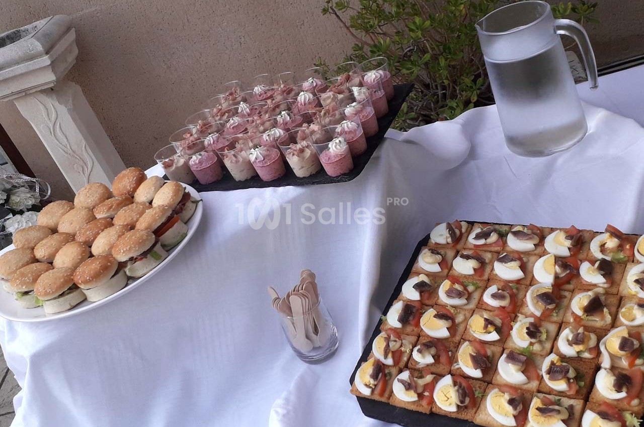 Plateau de mini-burgers, verrines sucrées et toasts garnis, disposés sur une table avec une carafe d'eau.