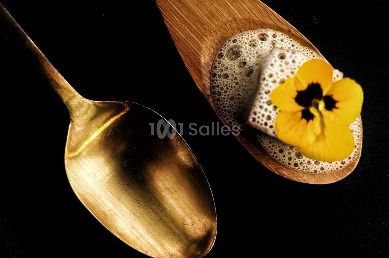 Cuillère dorée à côté d'une cuillère en bois contenant une mousse, un cube et une fleur jaune.