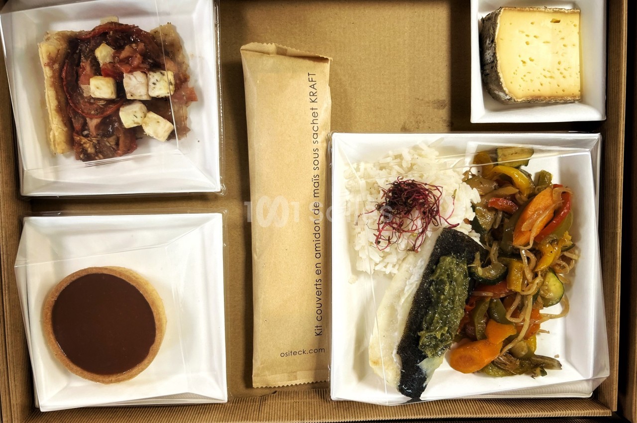 Plateau-repas composé de poisson, légumes, riz, tartelette, fromage, pain et couverts emballés dans un sachet kraft.