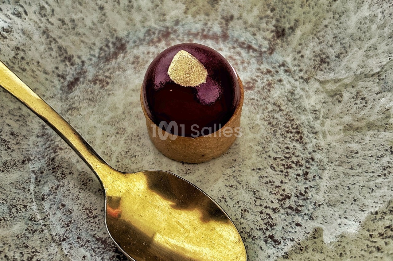 Dessert individuel au glaçage brillant rouge, décoré d'une touche dorée, présenté avec une cuillère dorée.