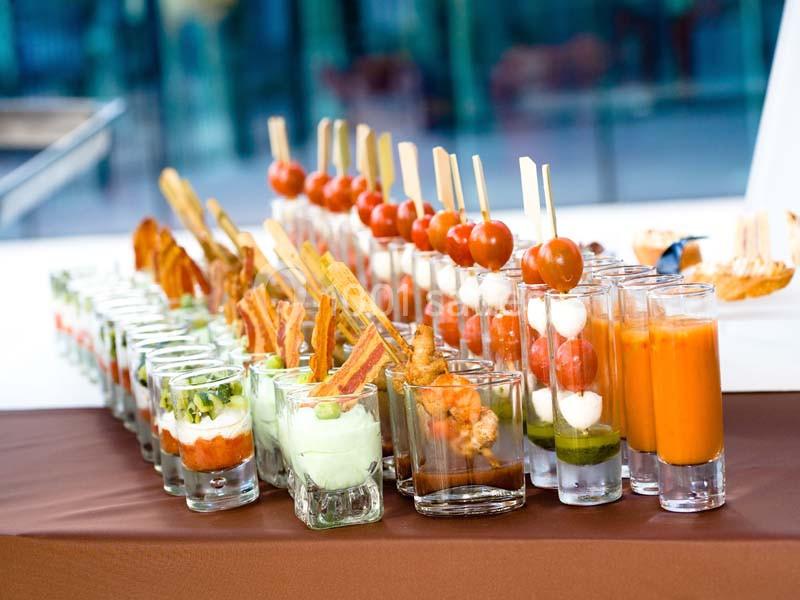 Buffet de verrines variées avec légumes, brochettes de tomates-mozzarella et soupes colorées sur une table.
