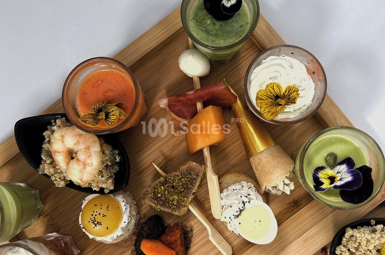 Plateau en bois avec une variété de verrines, bouchées salées et décorations florales comestibles.
