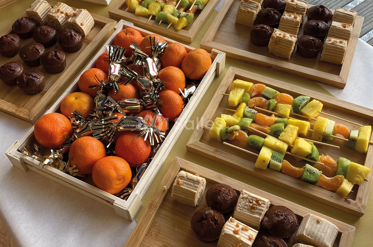 Plateaux en bois contenant des fruits frais, des pâtisseries et des friandises, disposés sur une table blanche.