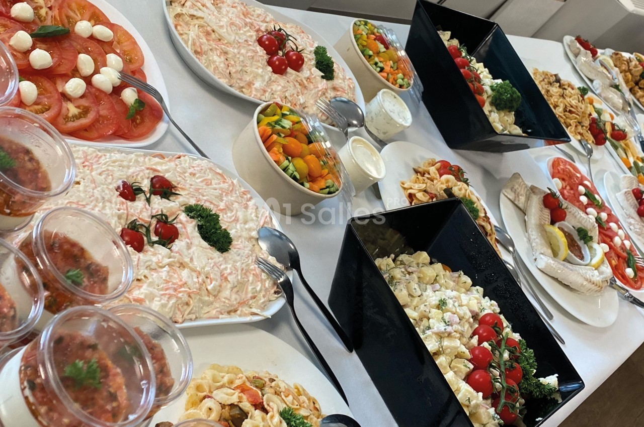 Buffet varié avec salades, légumes, pâtes, tomates, mozzarella et sauces disposés sur une table.