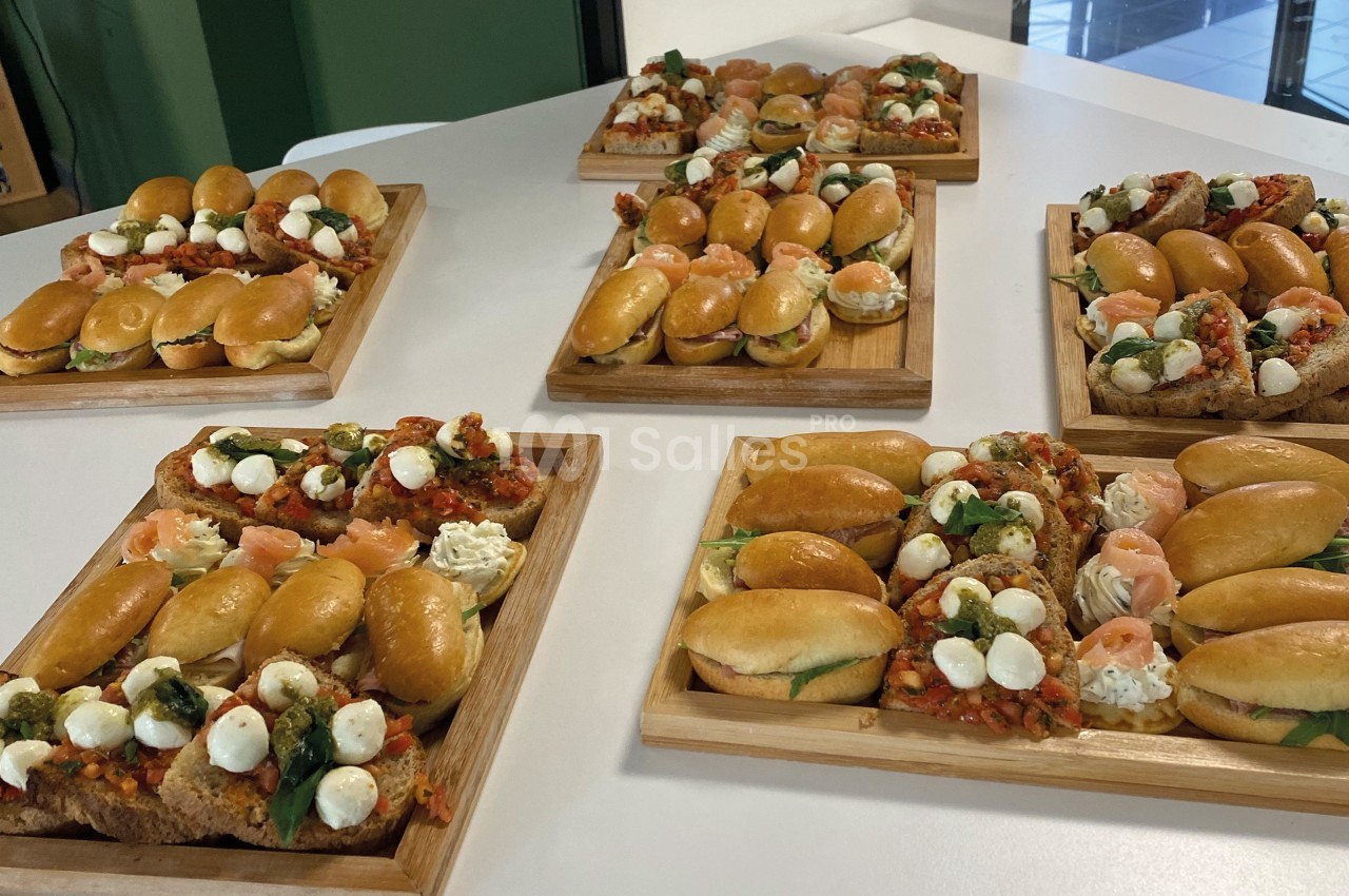 Plateaux en bois garnis de mini-sandwichs, bruschettas et bouchées variées disposés sur une table blanche.
