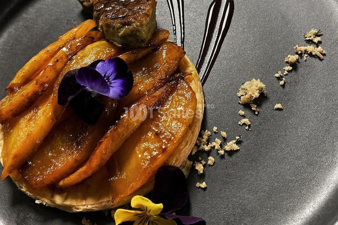 Tarte fine garnie de mangues caramélisées, décorée de fleurs comestibles et accompagnée d'une sauce au chocolat.