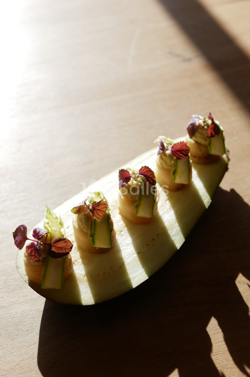 Tranche de courgette garnie de purée et décorée de petites feuilles et légumes, posée sur une table en bois.