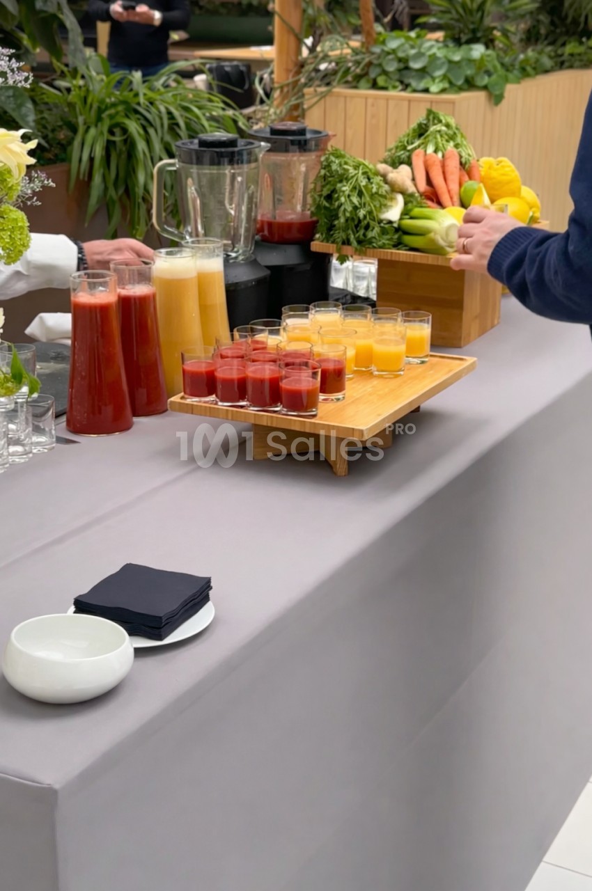 Buffet avec jus de fruits frais en carafes et en verrines, entouré de légumes et fruits sur une table grise.